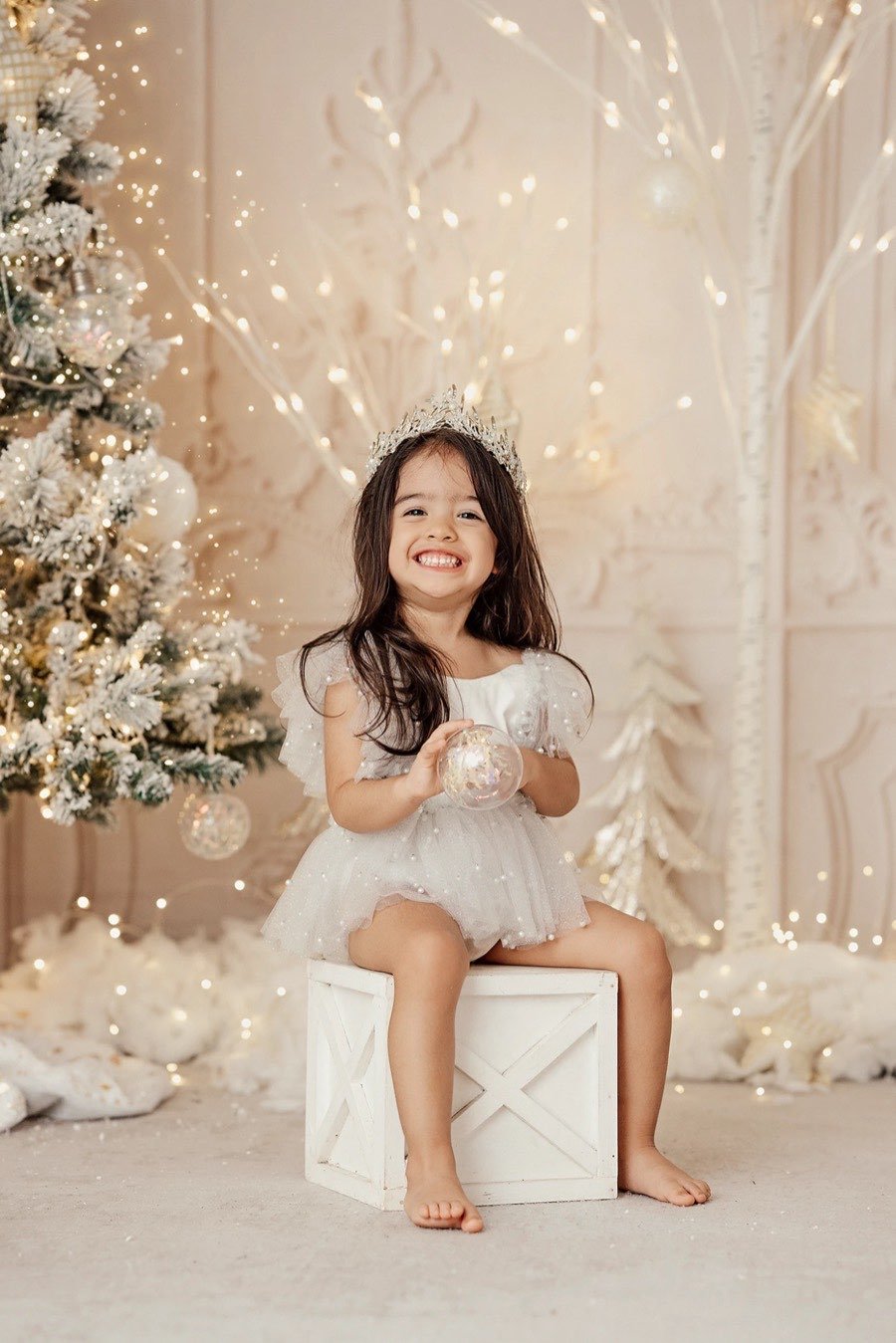 Niña con corona sentada en un cajón blanco, riendo