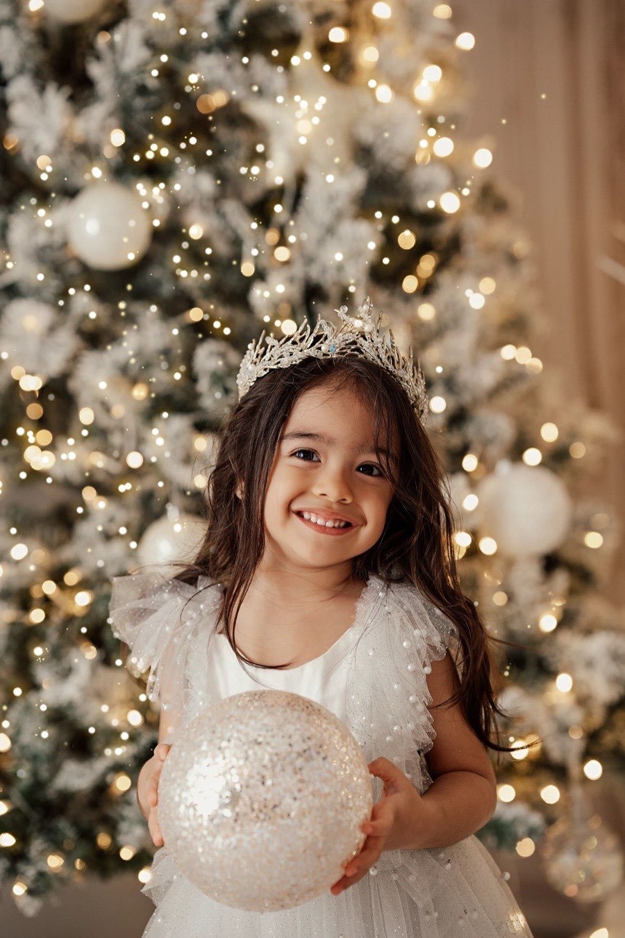 Niña sonriendo con una esfera frente al árbol iluminado
